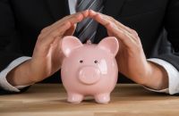 Złożone dłonie nad świnką skarbonką