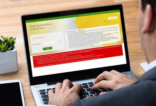 mężczyzna w garniturze piszący na klawiaturze laptopa, na ekranie laptopa widać ekran logowania