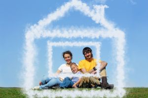 RODZINA 3 OSOBOWA, tata, mama i synek siedzący na łące, uśmiechnięci, tło niebieskie, rodzina w chmurze w kształcie domu